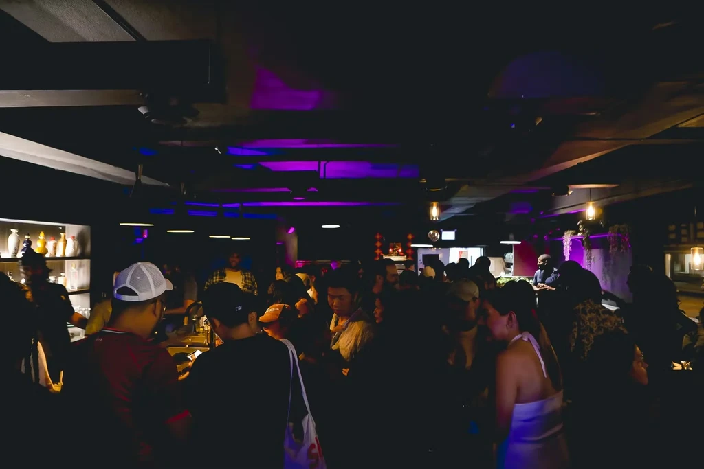 Crowded, dimly lit bar interior with purple and blue LED lights.