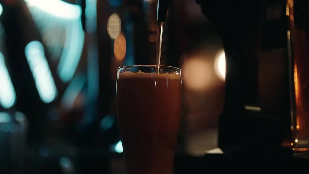 Amber beer pours from tap into glass, blurred background lights.