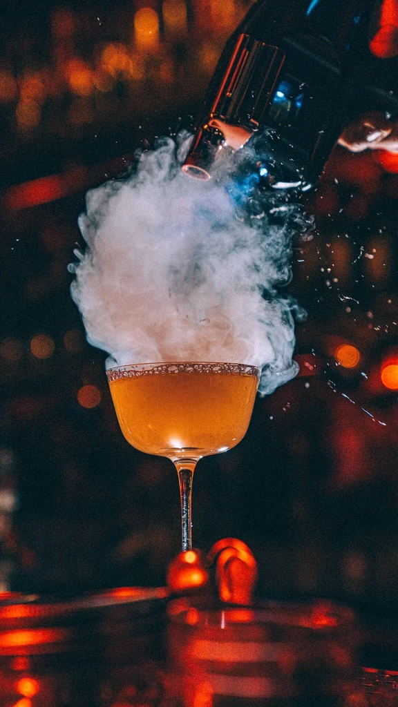 Orange cocktail in coupe glass with thick white smoke billowing over it.