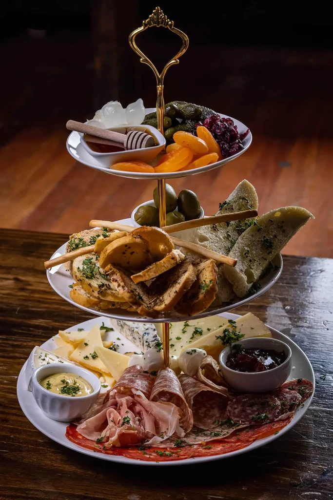Ornate three-tier platter with charcuterie, cheeses, fruits, and bread.