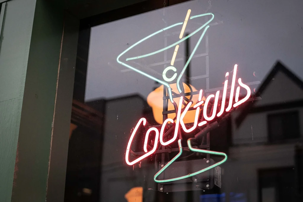 Neon sign of blue martini glass and pink "Cocktails" through window.