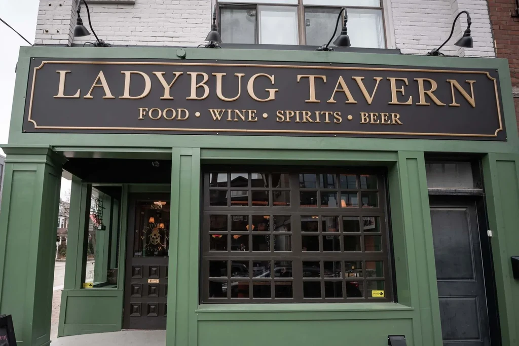Ladybug Tavern exterior, dark green building with illuminated bronze sign.