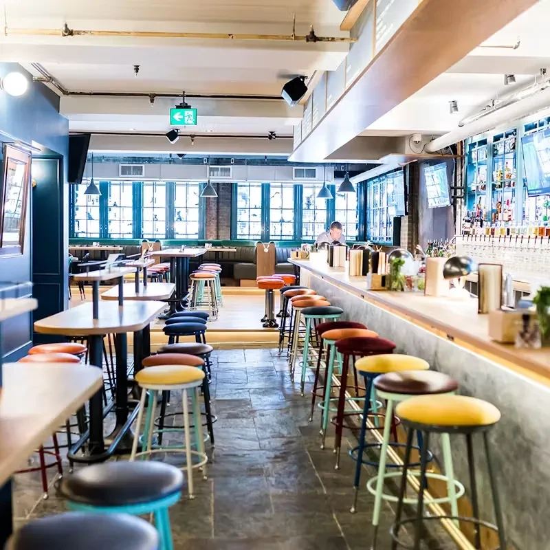 Modern bar and restaurant interior with colorful stools and dining area.