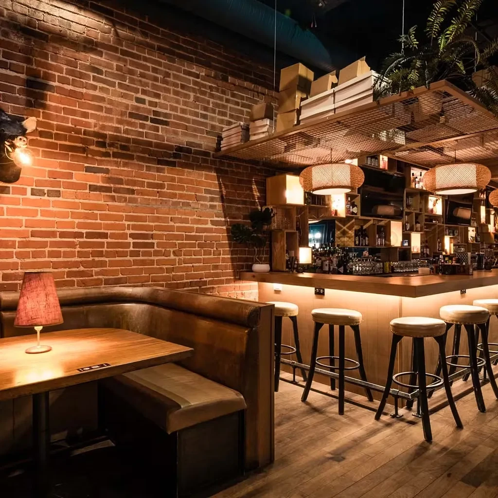 Warm, rustic modern restaurant interior featuring booth and illuminated bar.