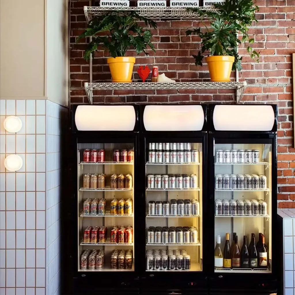 Three glass refrigerators displaying drinks against a brick wall with brewing signs.