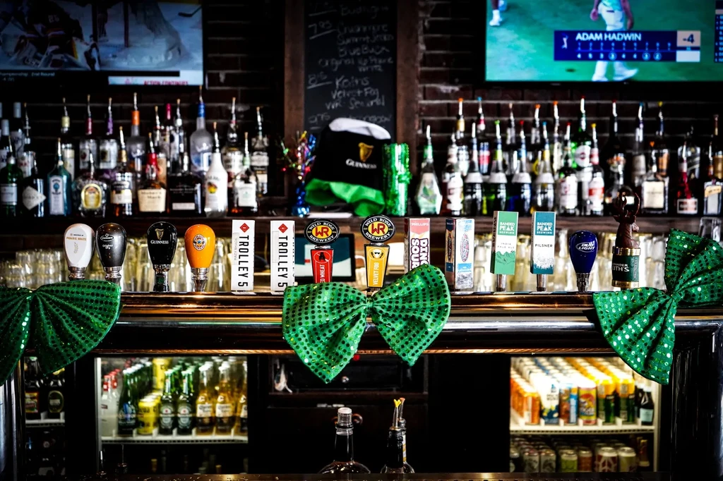 Bar with many beer taps, liquor bottles, green bows, and sports on TV.