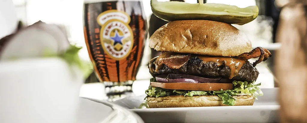 Gourmet bacon burger with pickle and a Newcastle Brown Ale.