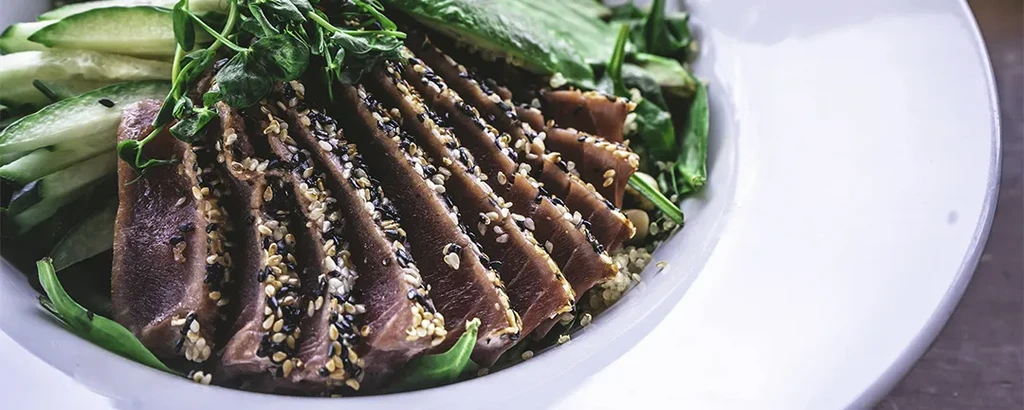 Seared sesame-crusted tuna on grain with vegetables, cucumber, and microgreens.