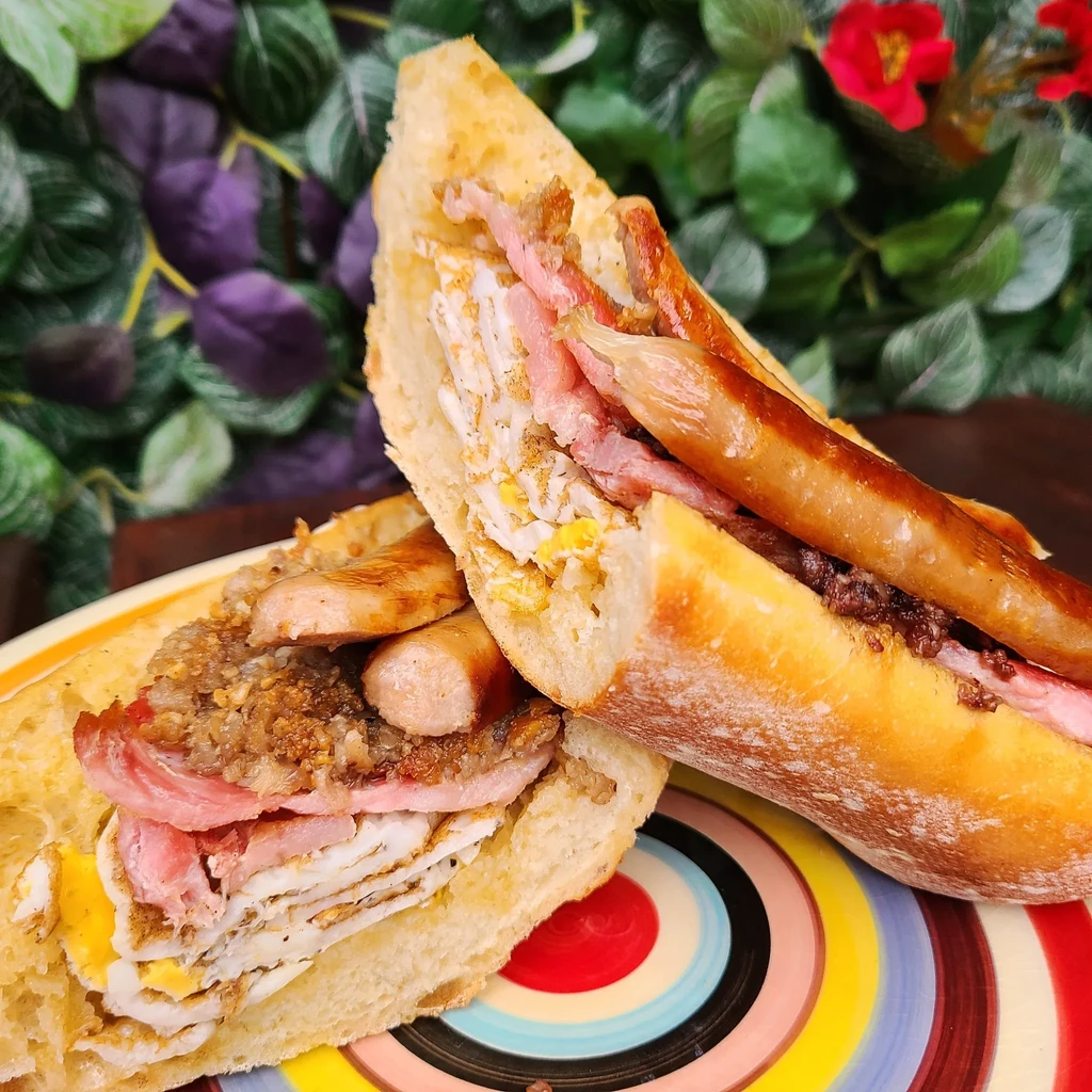 Full English breakfast baguette on a vibrant plate in a garden.