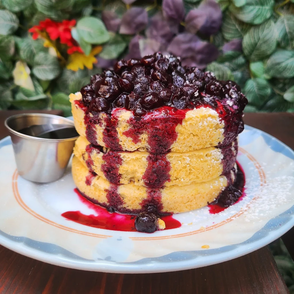 Fluffy pancakes topped with blueberry compote, powdered sugar, and syrup cup.