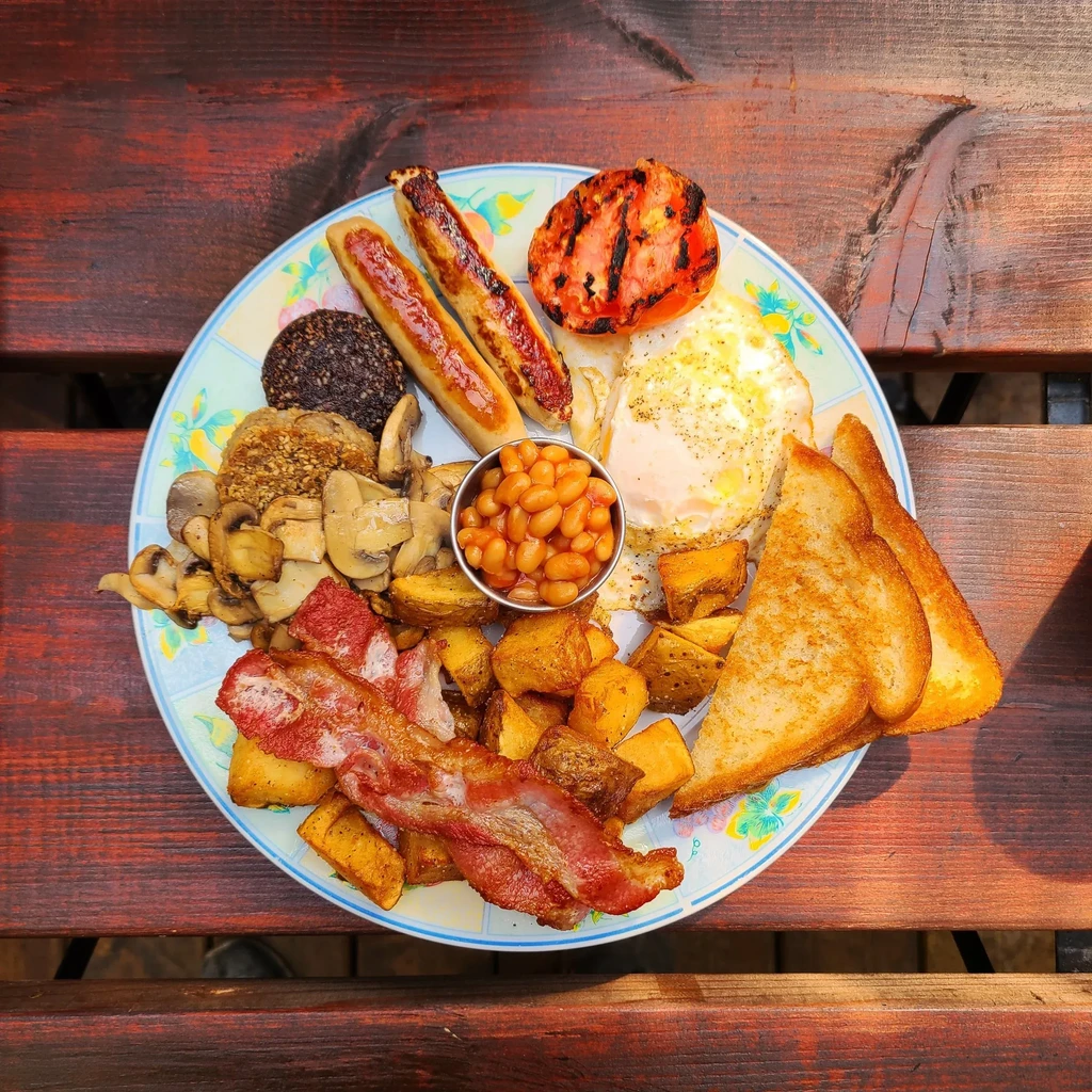 Overhead full English breakfast with sausages, eggs, bacon, beans, and toast.