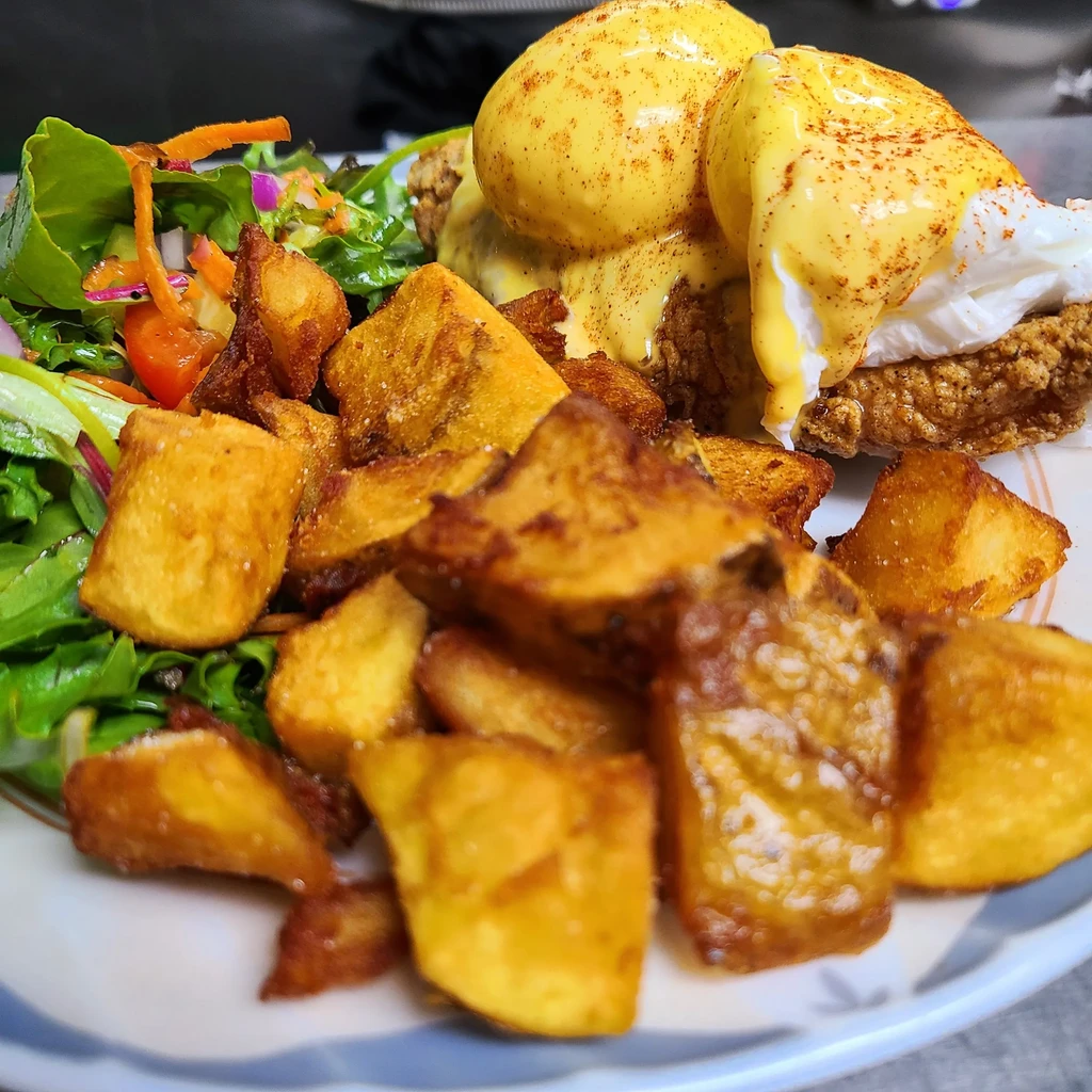 Plate of fried chicken, poached eggs with hollandaise, home fries, and salad.