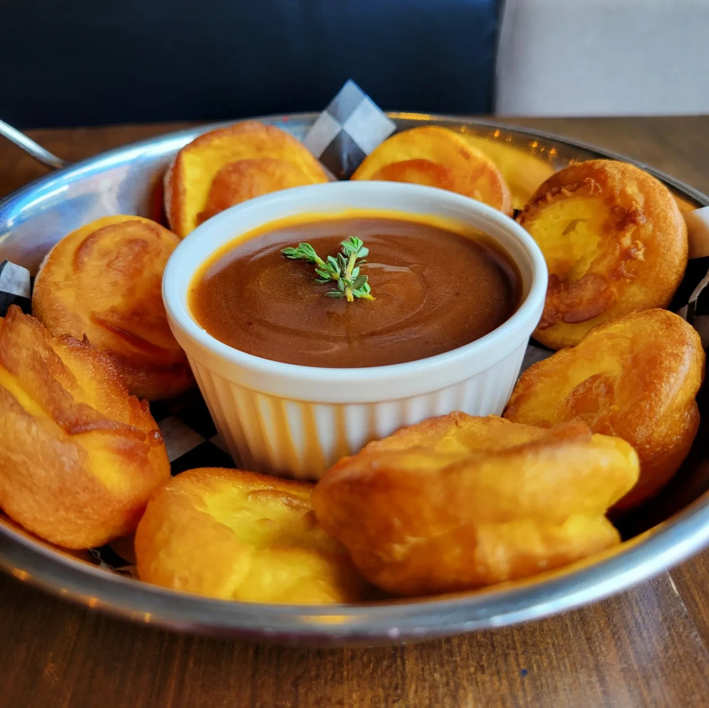 Golden Yorkshire puddings surround dark gravy in a thyme-garnished ramekin.