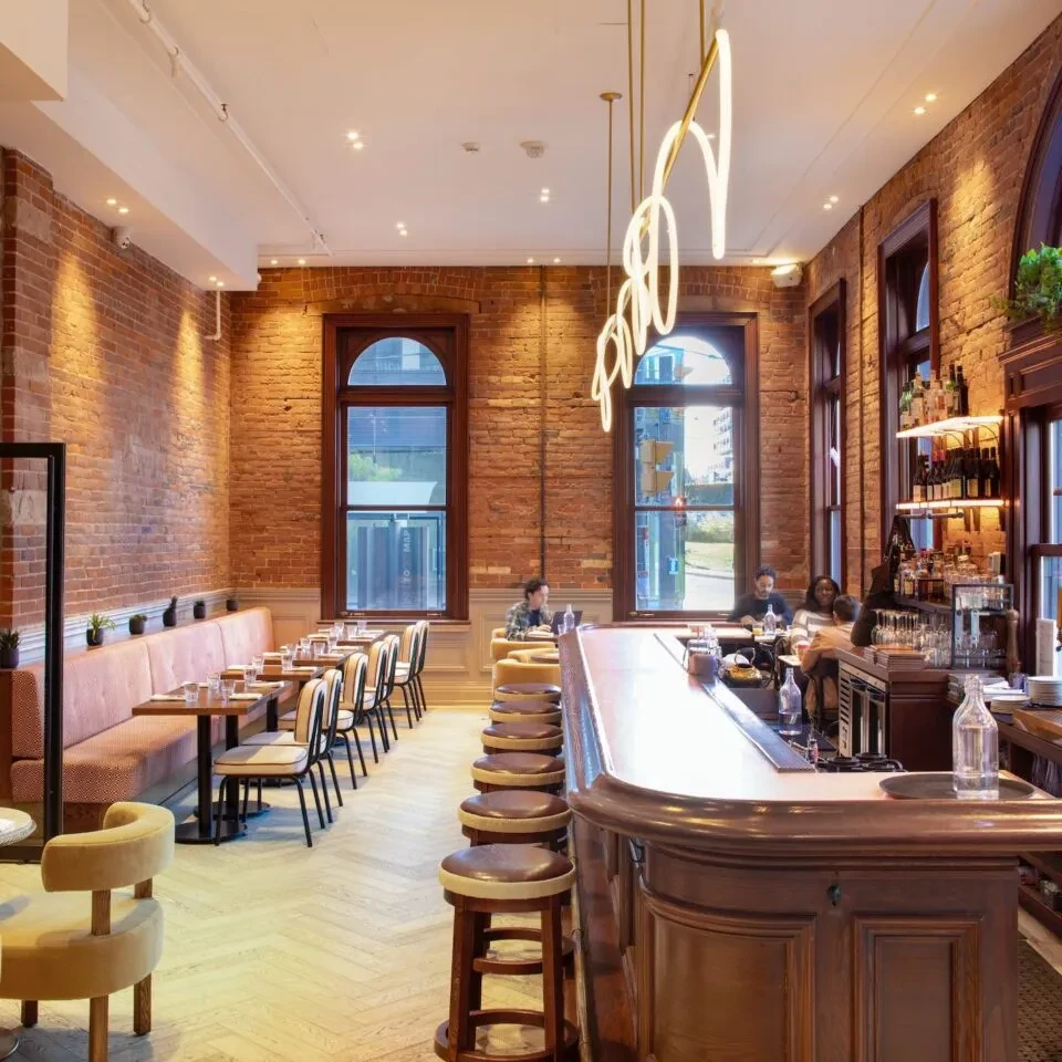 Restaurant interior: dark wood bar, peach banquette, brick walls, arched windows.