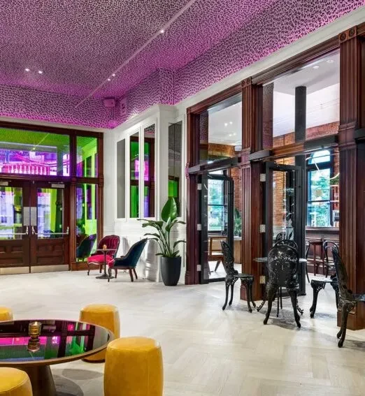 Eclectic modern lounge with magenta ceiling, yellow stools, and brick walls.