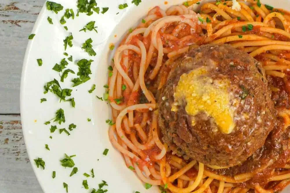 Spaghetti with large meatball, tomato sauce, cheese, and green herbs.
