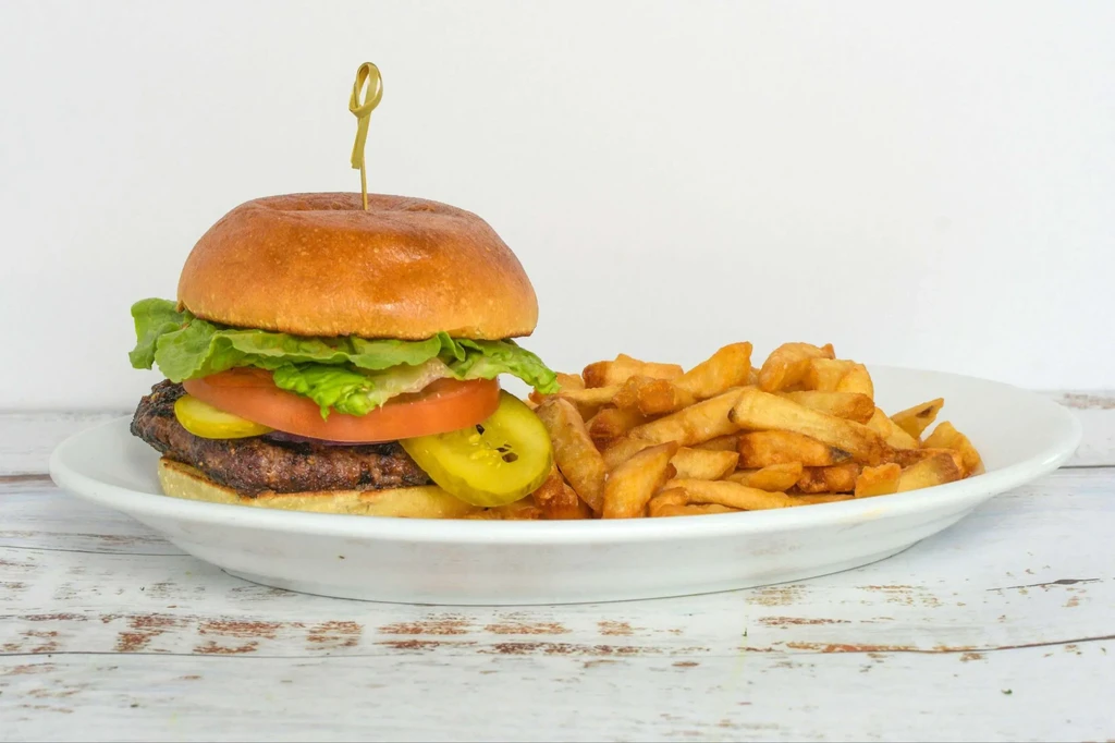 Close-up of a classic cheeseburger and crinkle-cut fries on a white plate.
