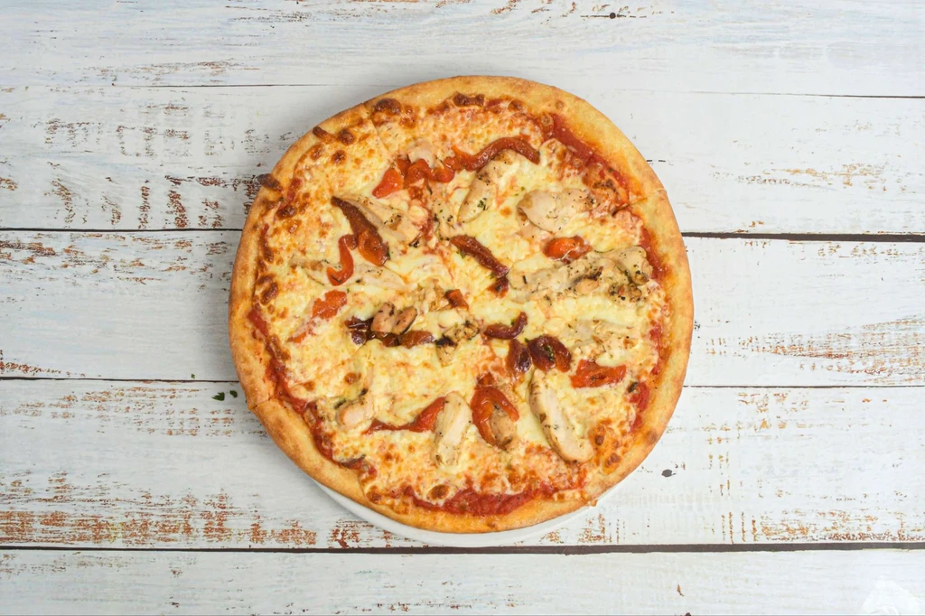 Whole pizza with chicken, sun-dried tomatoes, mozzarella on white wood.