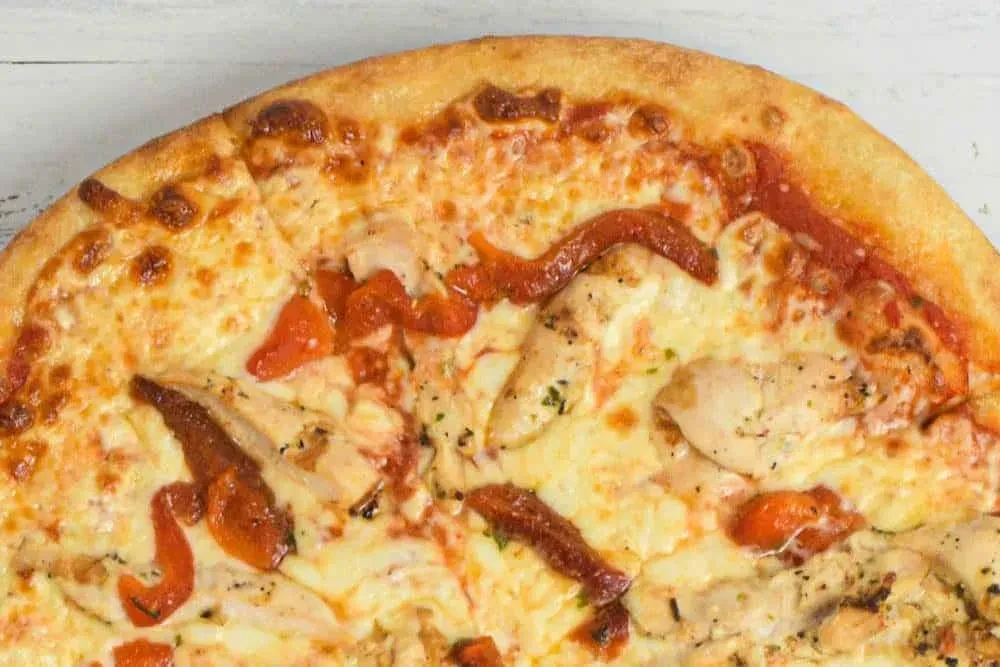 Freshly baked pizza with chicken, melted cheese, red peppers, and herbs.