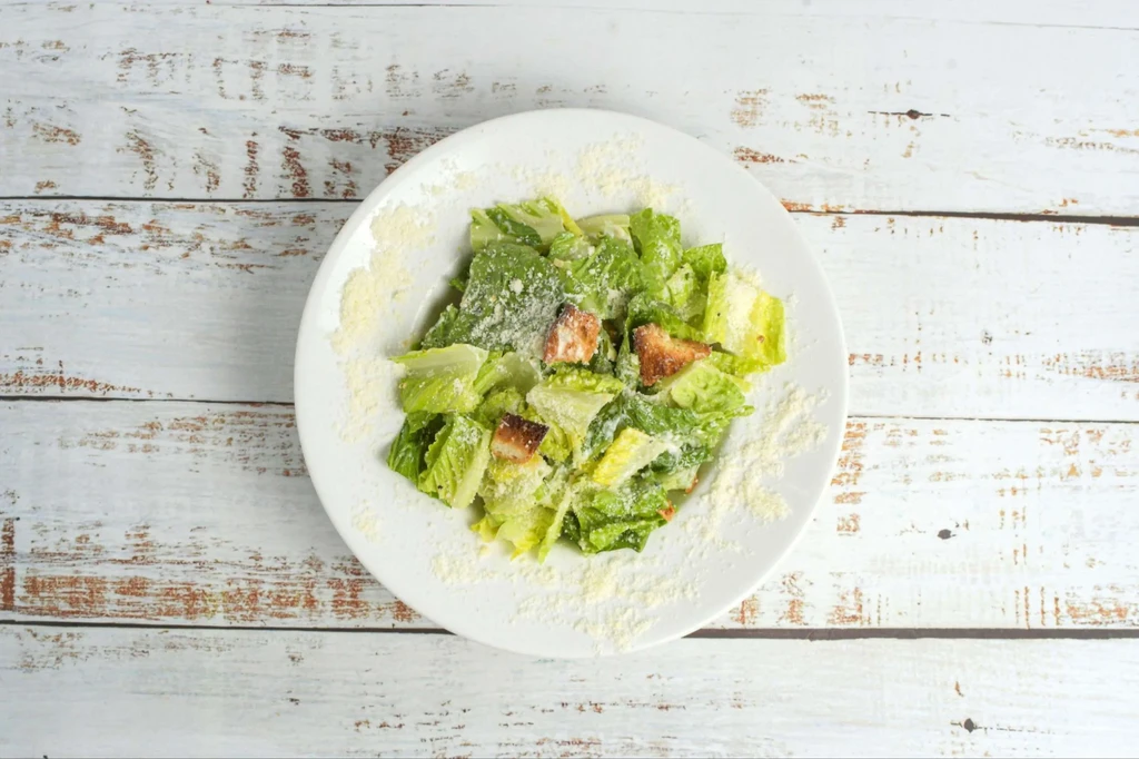 Caesar salad with romaine, croutons, and Parmesan on a wooden table.