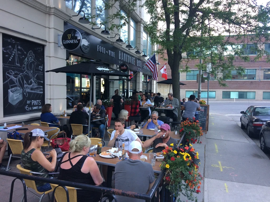 Banknote's lively patio, patrons, $6 pints special, and city street.