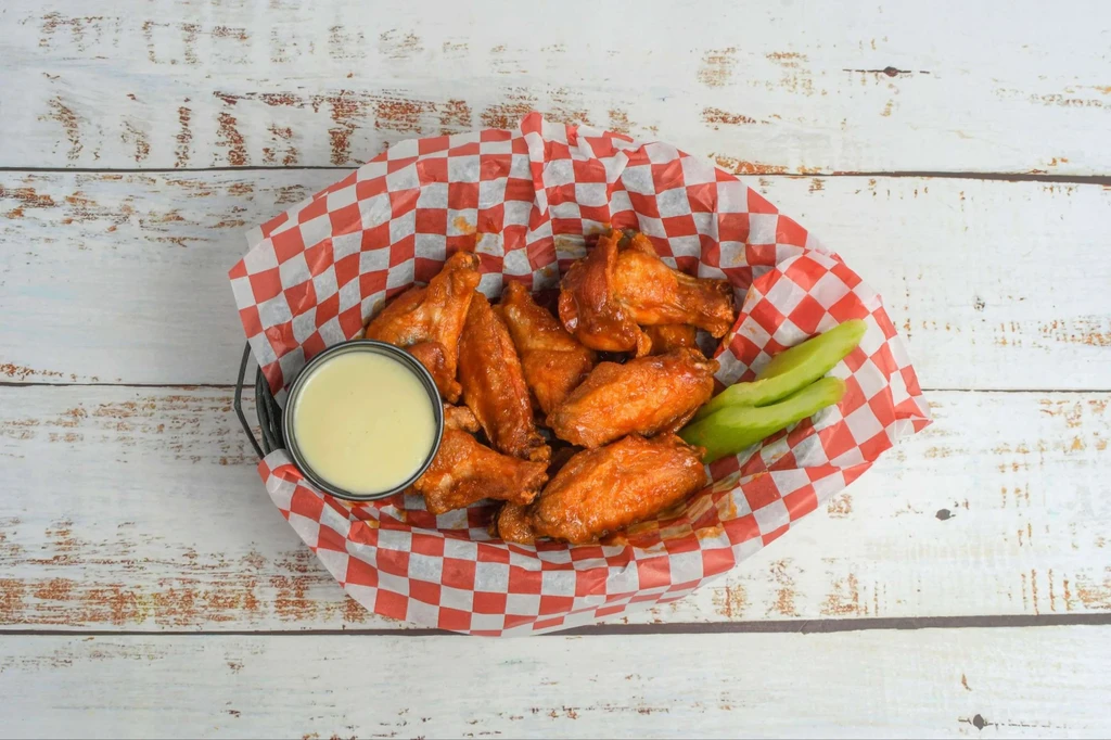 Buffalo chicken wings in a basket with dipping sauce and celery.