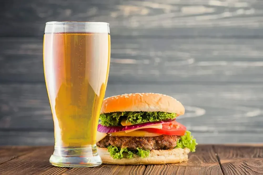 A golden beer and a cheeseburger on a rustic wooden table.