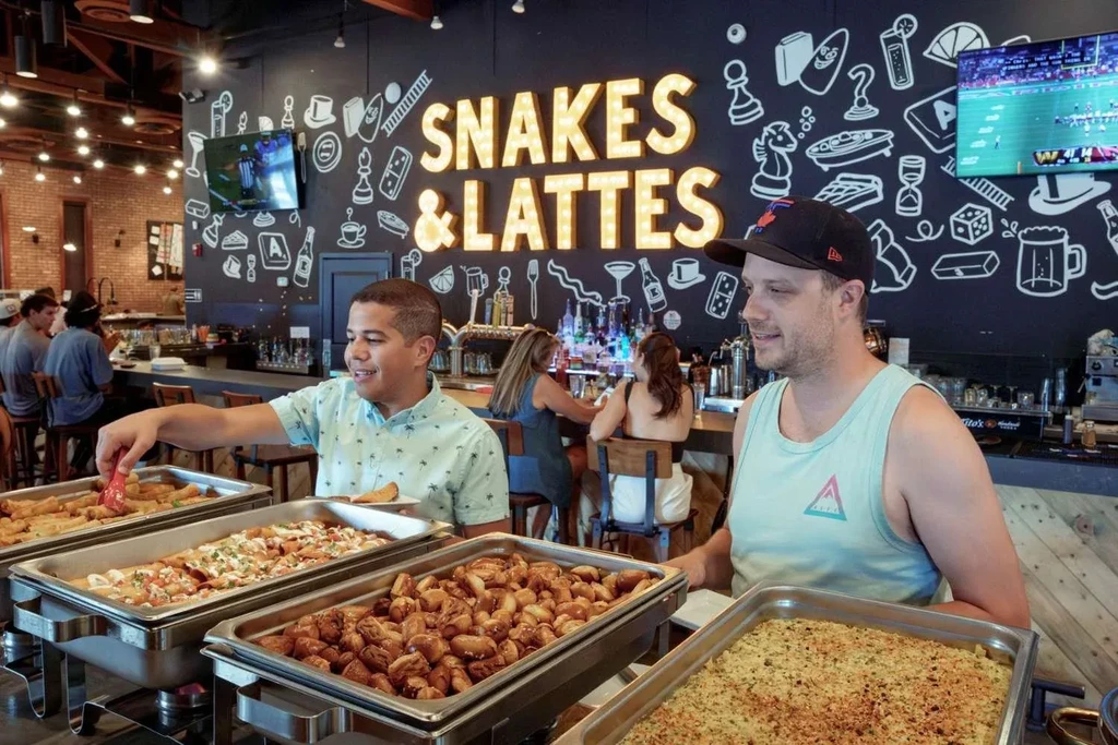 Men serving themselves food at a buffet in Snakes & Lattes cafe.