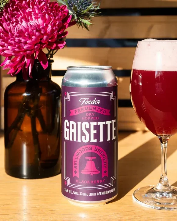 Bellwoods Blackberry Grisette beer can, glass, and vibrant pink flowers.