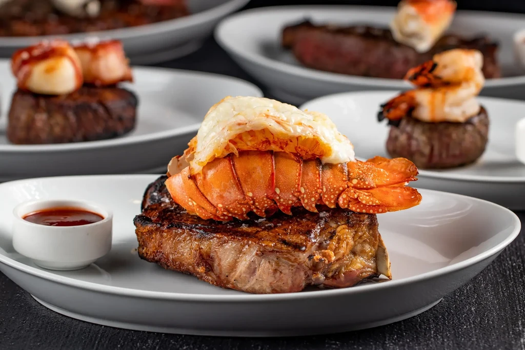 Seared steak with lobster tail among other surf and turf plates.