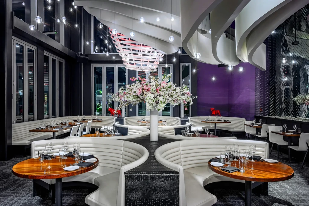 Elegant restaurant interior: wavy ceiling, spherical lights, white booths, set tables.