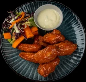 Plate of reddish-orange chicken wings, salad, and creamy dip.