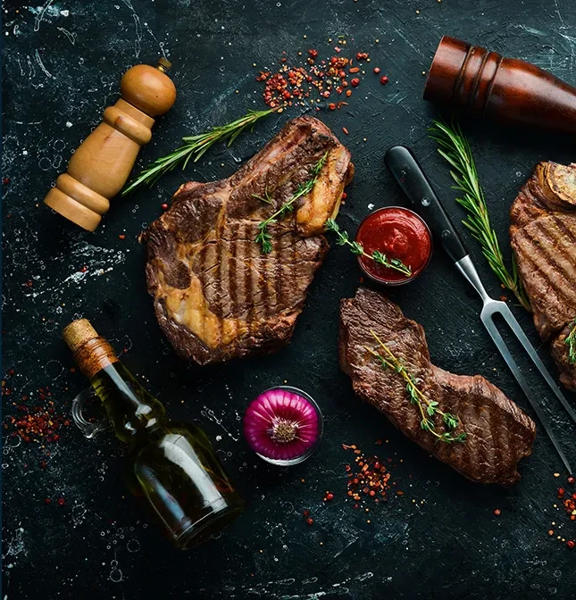 Three cooked steaks with sauce, rosemary, and utensils on a dark surface.