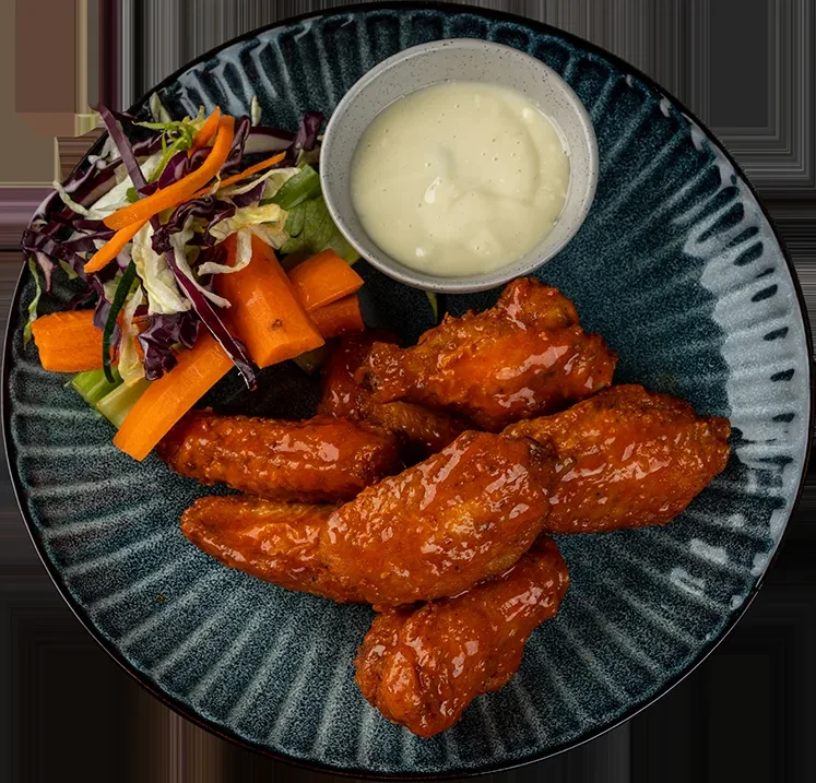 Five sauced chicken wings, fresh vegetables, and dip on dark plate.