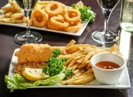 Two plates of golden fried fish, chips, onion rings, and drinks.