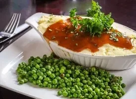 Mashed potato casserole with gravy, parsley, and peas in gratin dish.