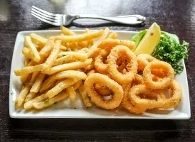 White plate with golden french fries, crispy calamari, lemon, and lettuce.