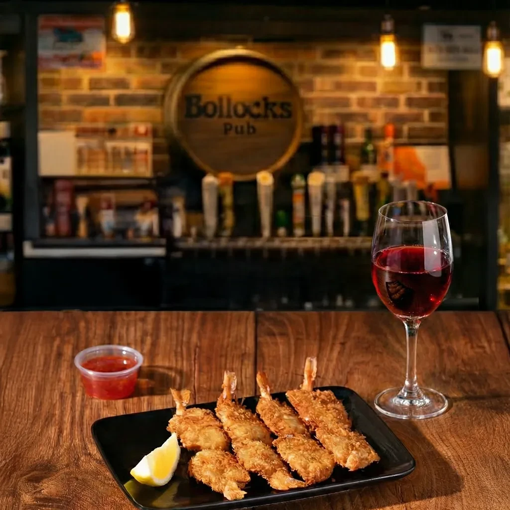 Fried shrimp, lemon, dipping sauce, and red wine on a pub bar.