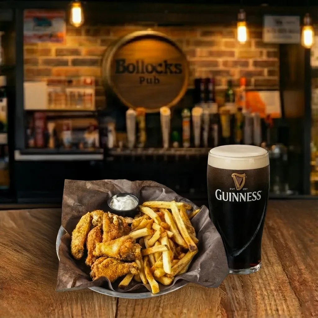Fried chicken wings, fries, and a Guinness pint on a rustic pub bar.