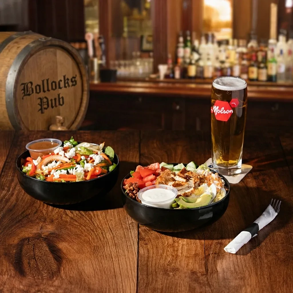 Two fresh salads and a Molson beer on a pub table.