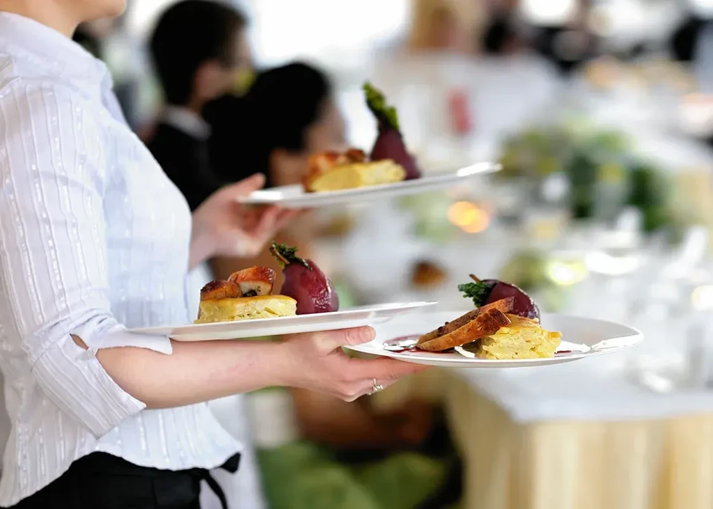 Server holding two white rectangular plates of beautifully plated dishes.