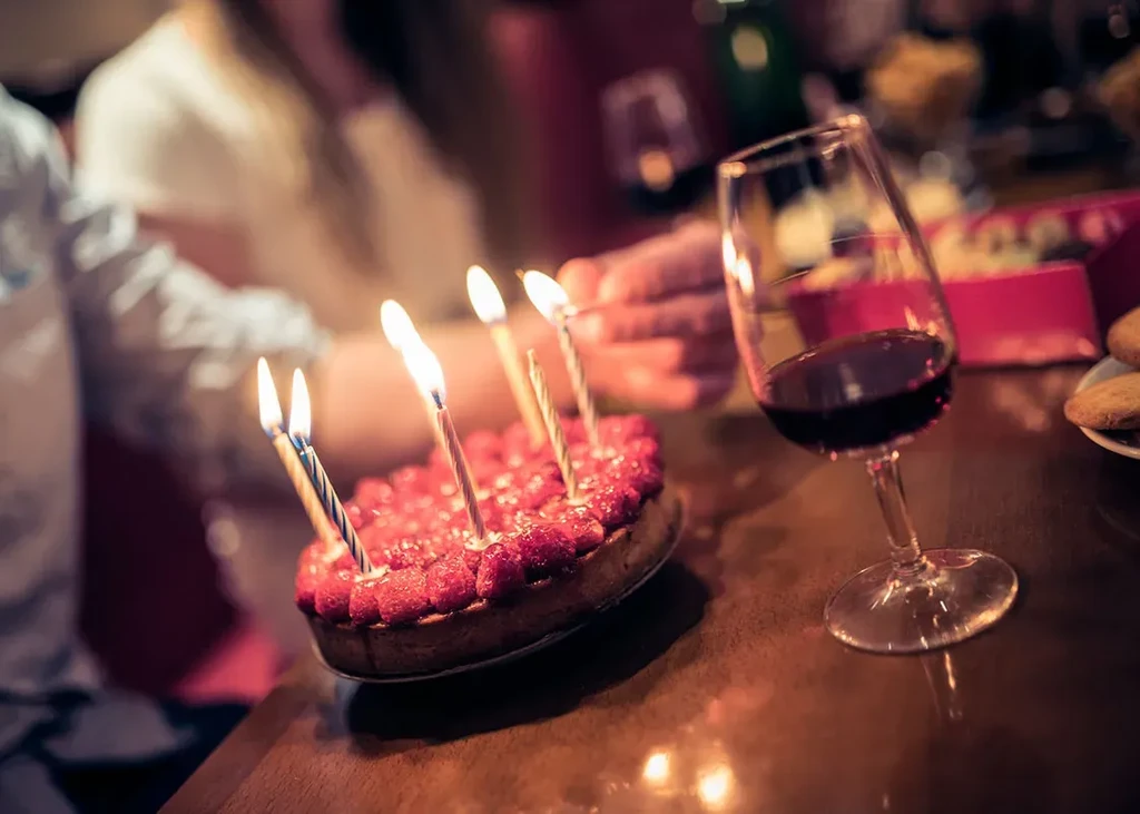 Dimly lit berry tart with lit birthday candles and red wine.
