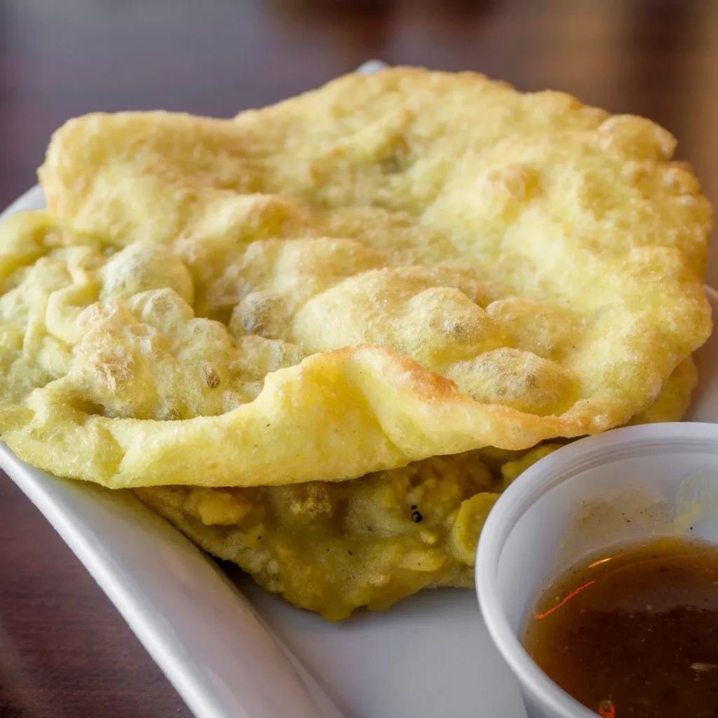 Stacked golden fritters with a cup of dark dipping sauce.