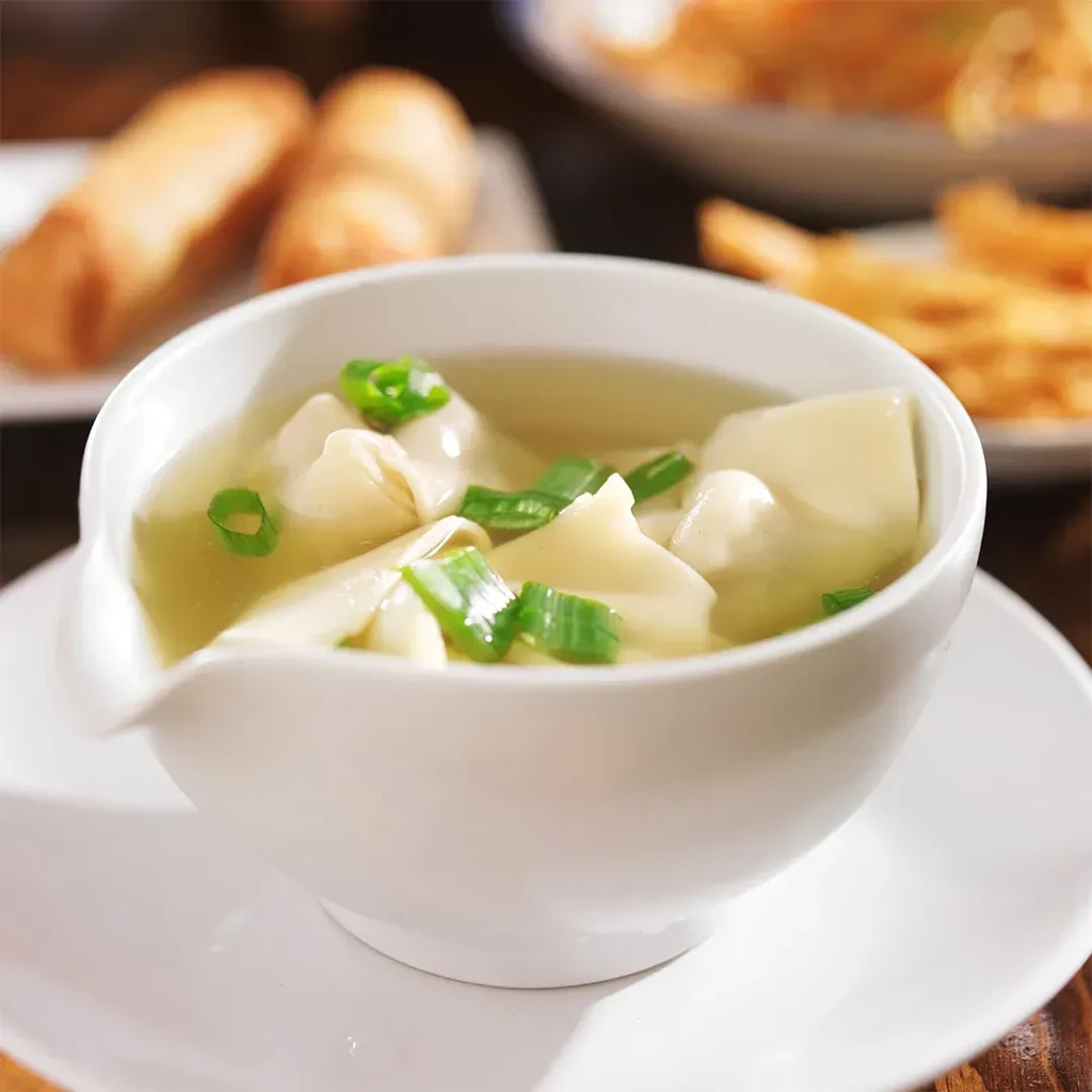 White bowl of wonton soup garnished with green onions.