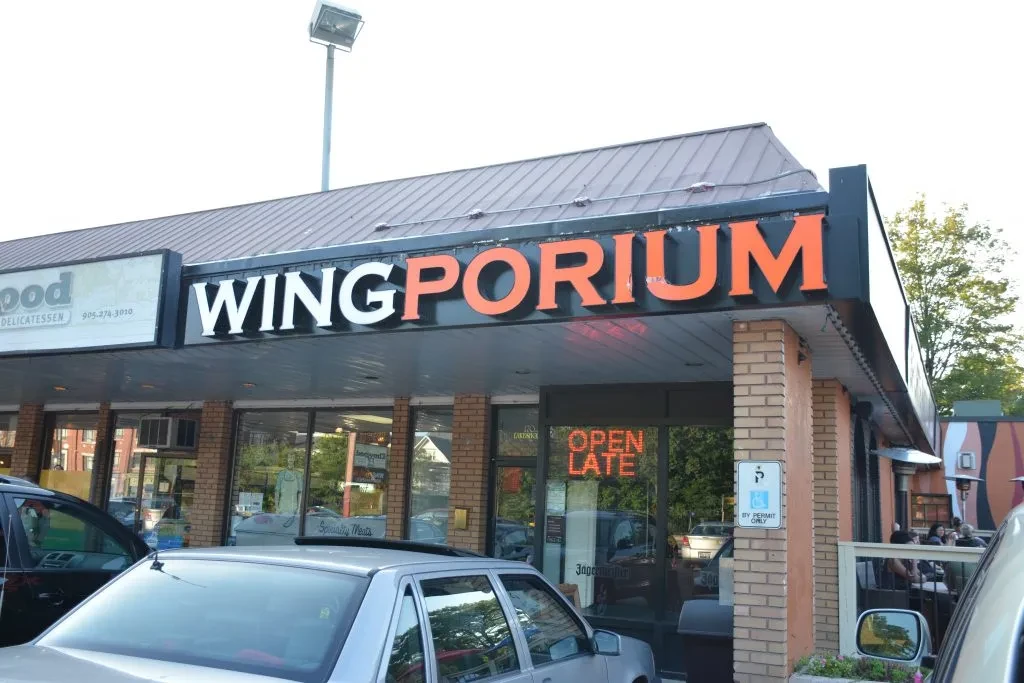 Exterior view of Wingporium restaurant with an outdoor patio and parked cars.