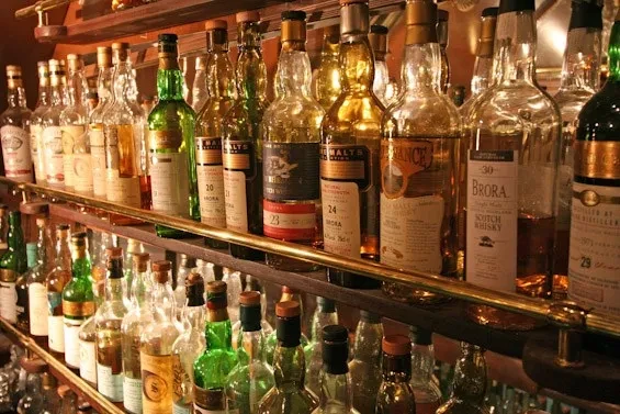 Well-stocked wooden bar shelves display many aged whisky and scotch bottles.