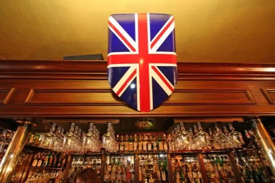 Dim British pub interior with Union Jack shield and stocked bar.
