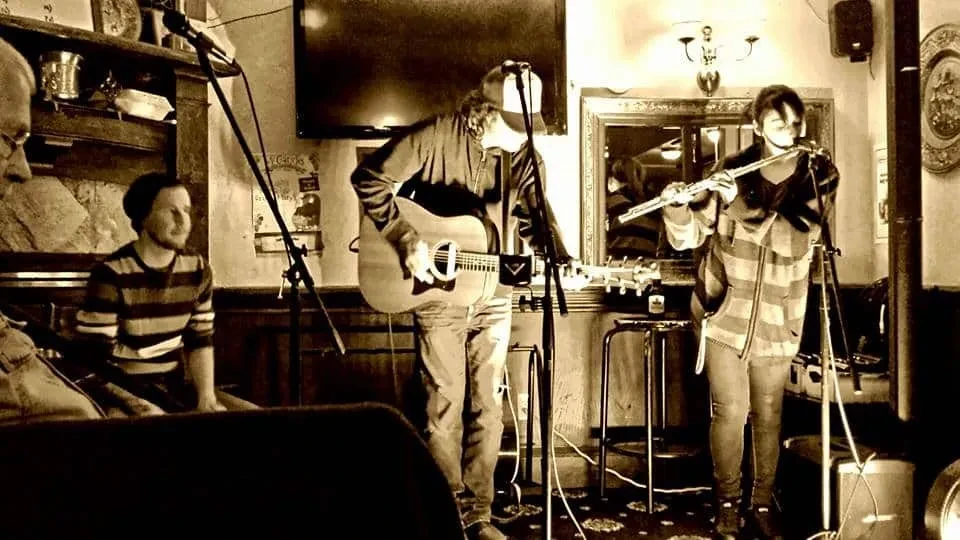 Two musicians performing live in a sepia-toned, dimly lit pub.