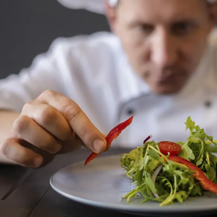 Chef's hand garnishes fresh vibrant salad with a red bell pepper.