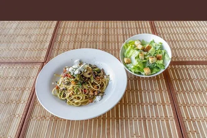 Pasta with vegetables and feta, and Caesar salad on bamboo.